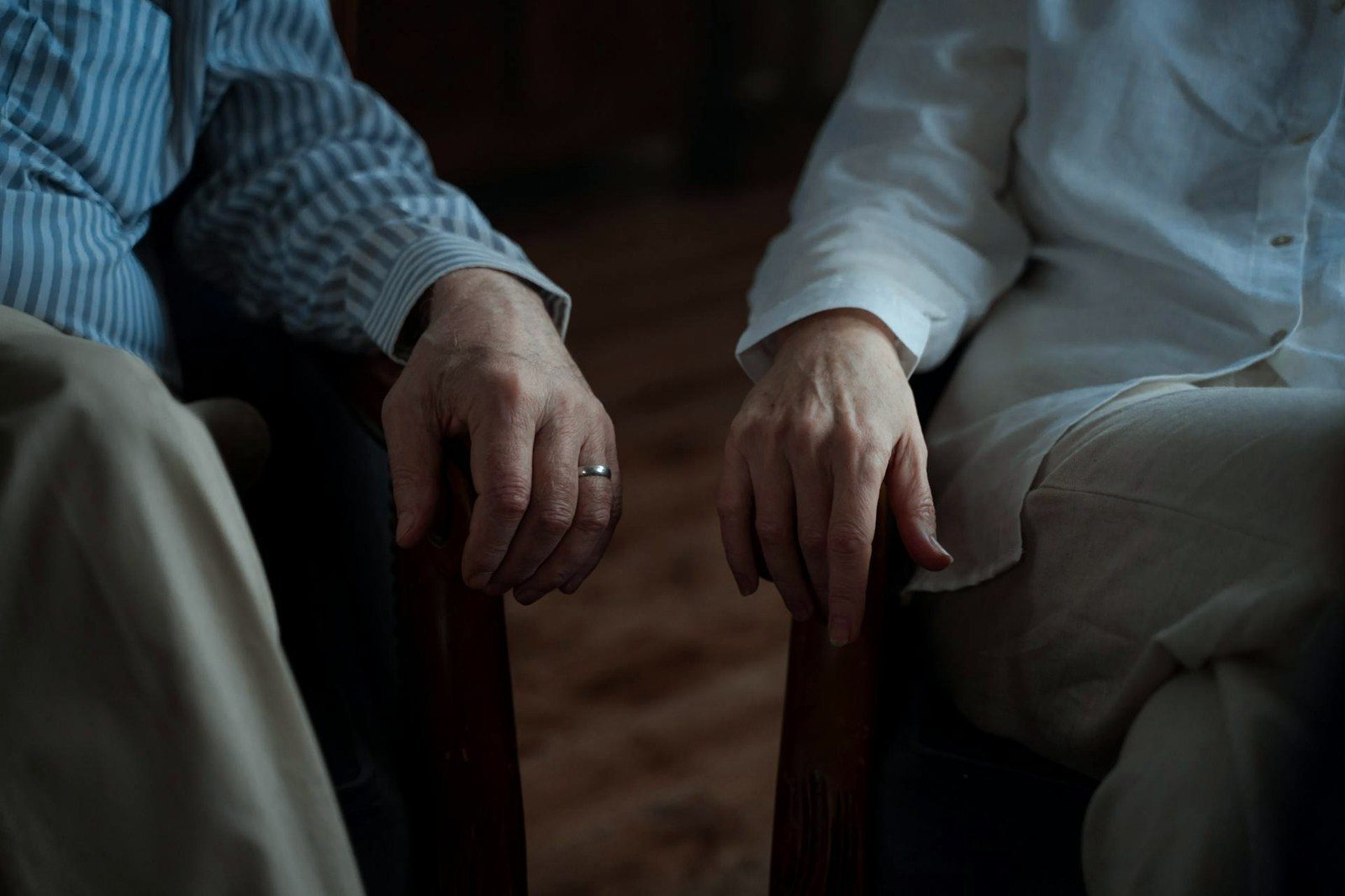 Two pairs of hands at rest on the arms of neighbouring chairs