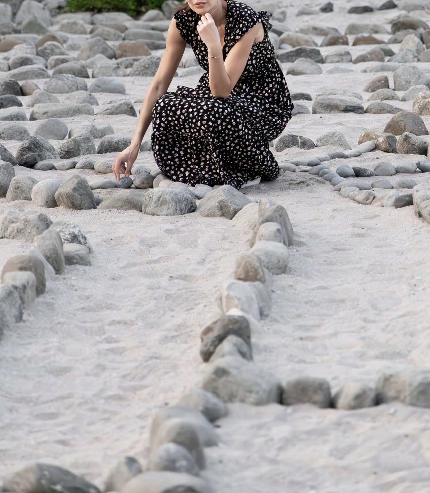 A figure seated within a spiral of stones laid on pale sand